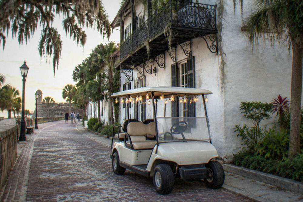 A small golf cart tour vehicle parked on a narrow brick lane beside a lantern-lit historic building