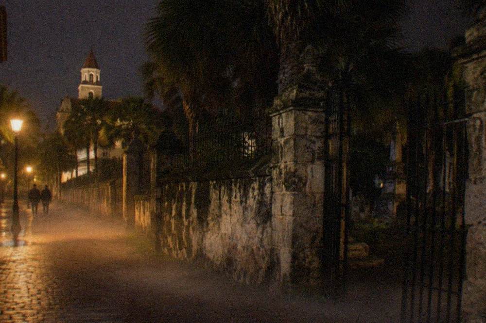 A narrow lamplit historic street at night with old coquina walls