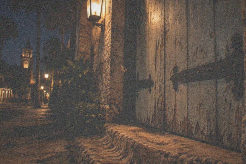 A weathered historic wooden door at night lit by a single lantern