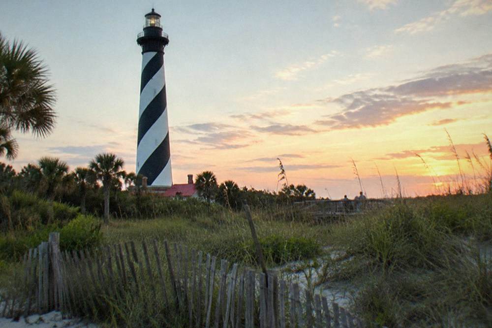 Black and white striped lighthouse tower against an evening sky over coastal dunes