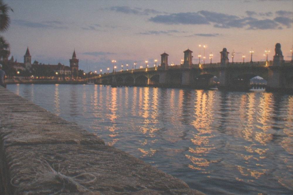 A historic waterfront seawall at twilight with a lit bridge in the distance