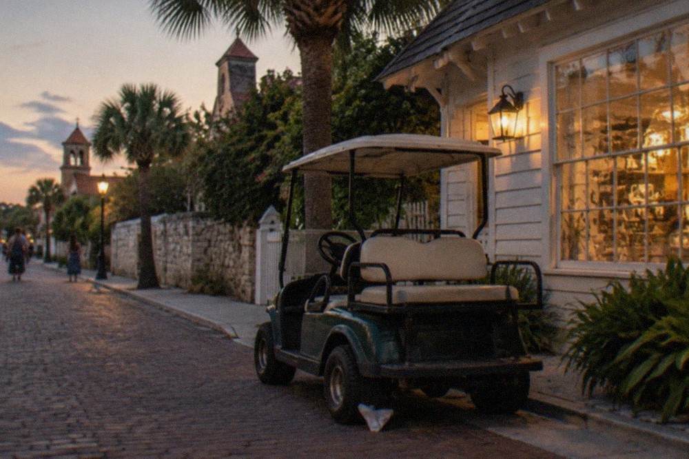 A small golf cart waiting at dusk beside a lit historic storefront on a narrow brick street