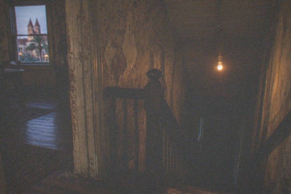 A dimly lit interior of an old wooden house with a staircase in shadow