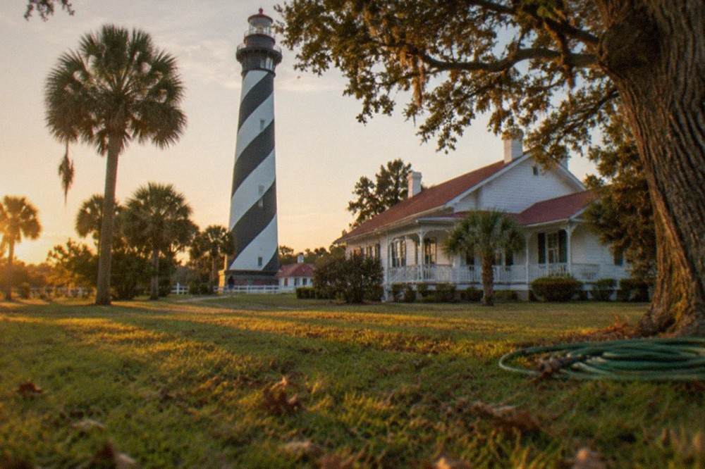 The black and white striped lighthouse tower and keeper's house seen across the lawn at golden hour